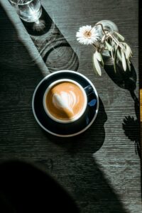 Cup of cappuccino coffee on black wooden table at cofffe shop. Lights and shadows, food photography
